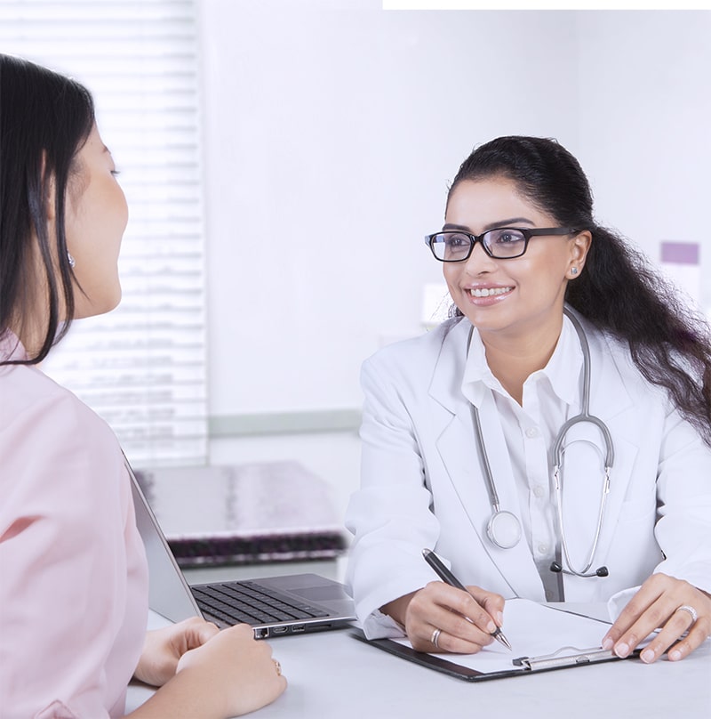 Image of female doctor sitting in her office with laptop and stethoscope while writing on the clipboard and listening her patient